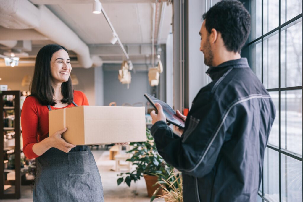 A friendly interaction takes place as a delivery courier delivers a box of goods to the organic store, with a staff member smiling and accepting the package with gratitude